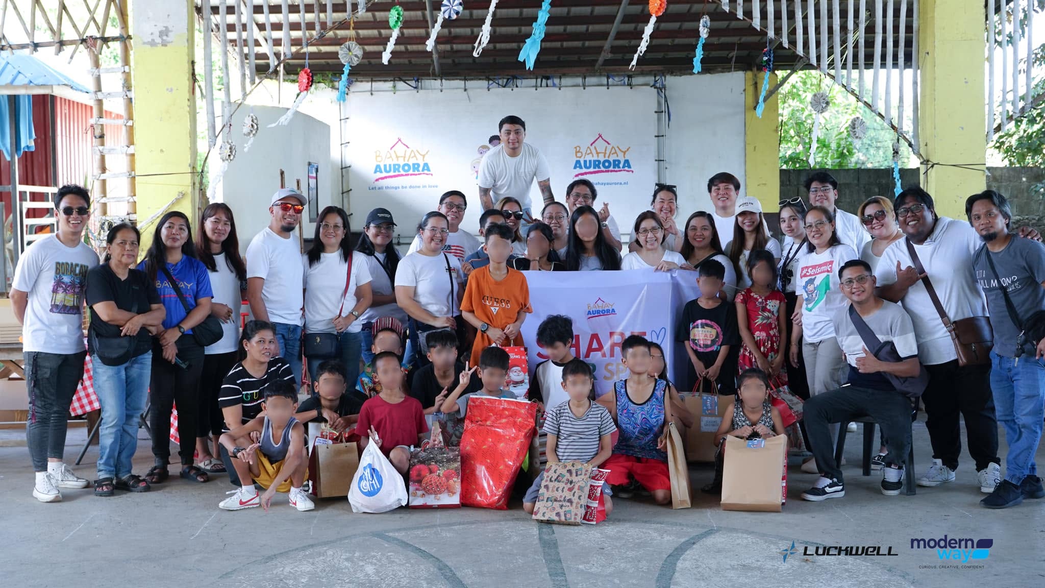 A group gathered at Bahay Aurora with children and gift bags; faces are blurred in the supplied photograph.