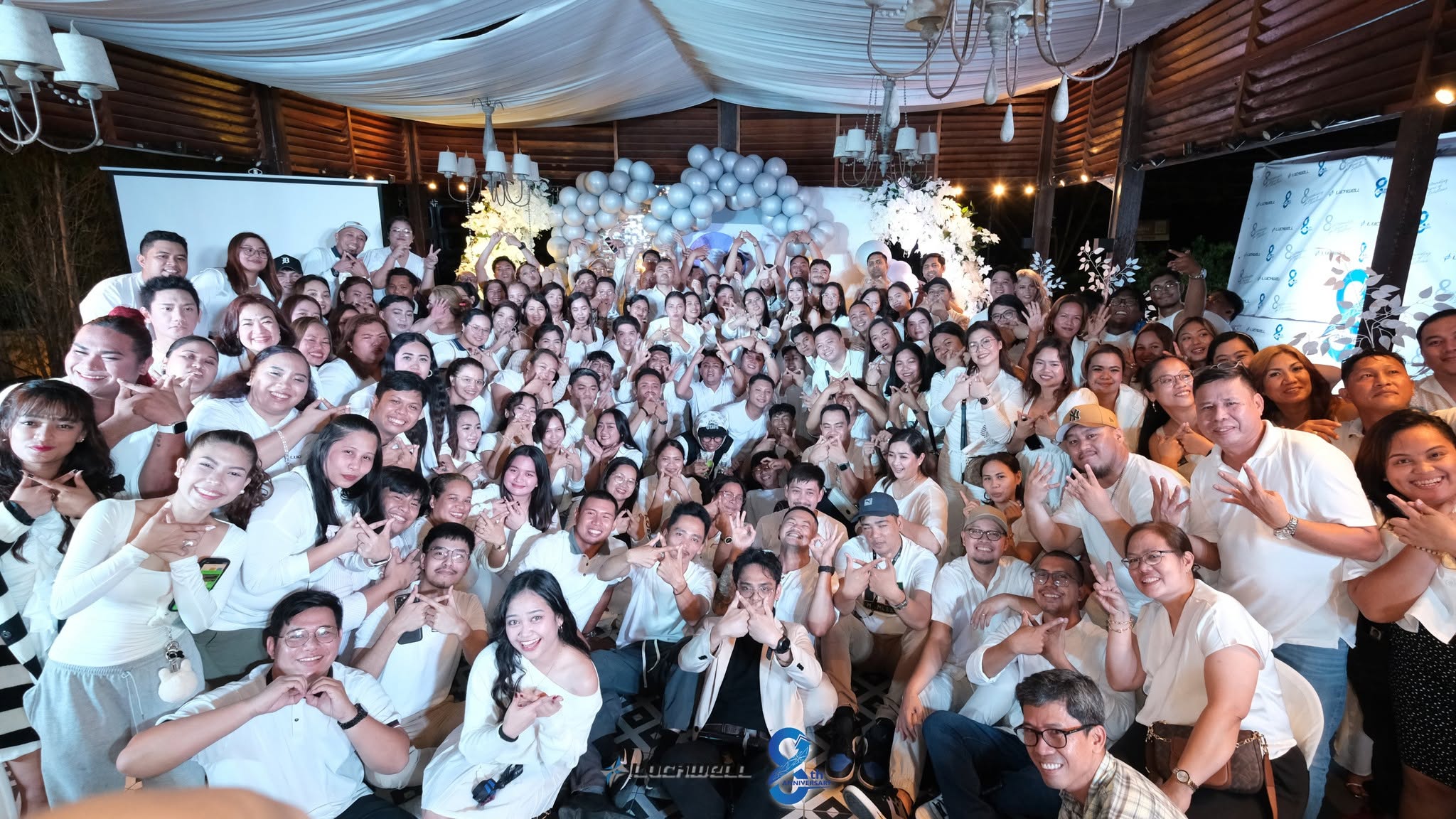 A large group in white clothing posing together at an indoor celebration.